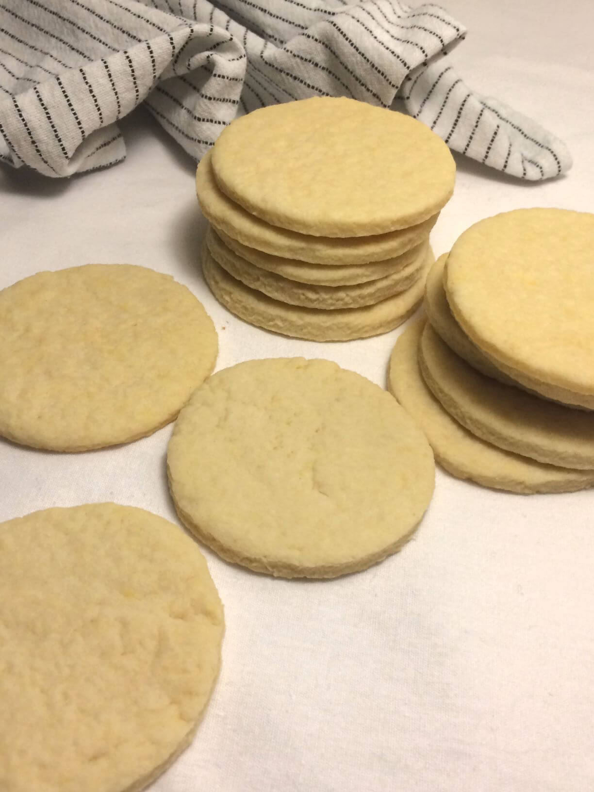 baked cut out sugar cookies with 2 stacks and 3 single cookies in the front with a white towel with black strips in the back