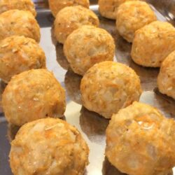 thre rows of sweet potato and turkey meatballs lined up on a stianless steel baking sheet close up view