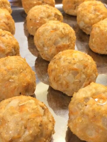 thre rows of sweet potato and turkey meatballs lined up on a stianless steel baking sheet close up view