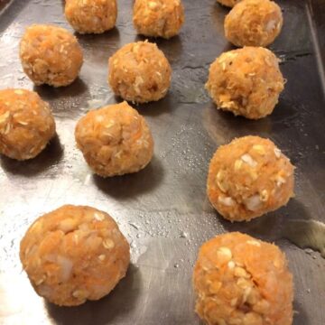 raw meatballs lined up on stainless steel baking sheet on olive oil