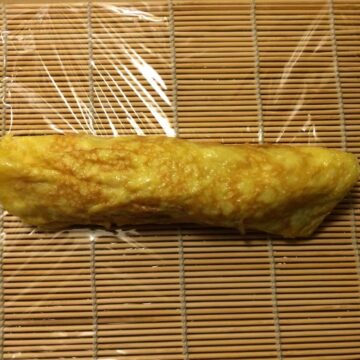Tamago rolled up on sushi mat covered in Saran wrap.