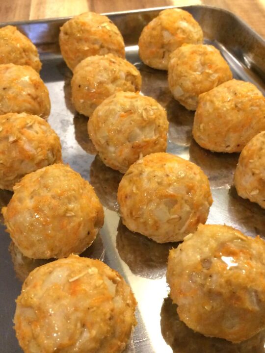 3 rows of sweet potato turkey meatballs lined up on a stainless steel baking sheet, angled to the left all on a wooden cutting board