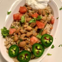 white oval Corning Ware bowl filled with cooked barley, pinto bean mixture, freshly sliced jalapeno, chopped cilantro, diced tomato, and Greek yogurt