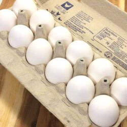 egg carton filled with 12 eggs on a wooden cutting board