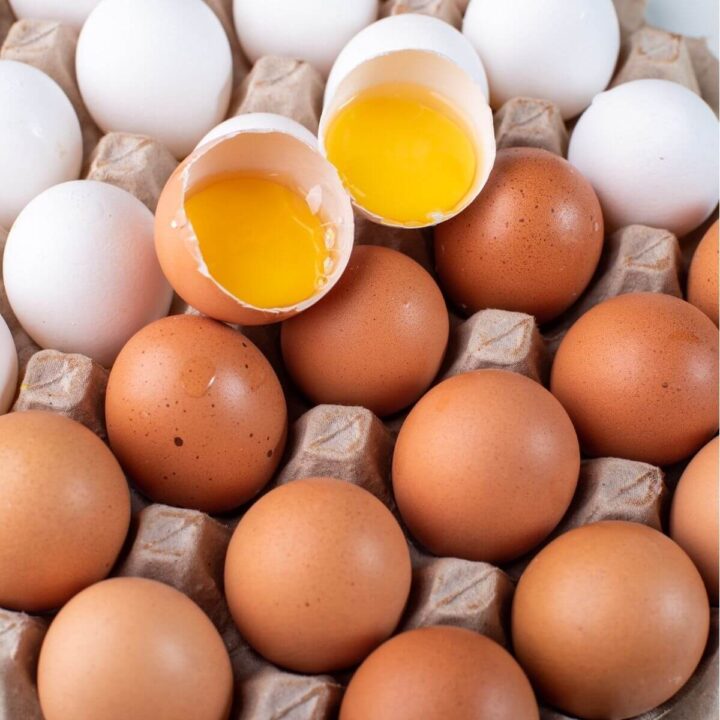 open carton of brown eggs and white eggs with 2 halves cracked open each with egg yolks.