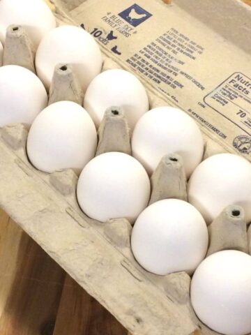 egg carton filled with 12 eggs on a wooden cutting board