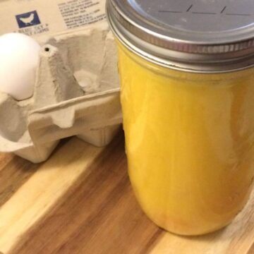 egg carton showing 1 egg with tall mason jar with lid and ring filled with blended eggs, all on a wooden cutting board