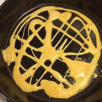 laced pancake batter drizzled in haphazard pattern on cast iron skillet