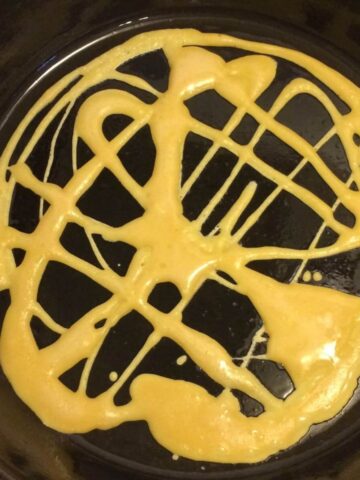 laced pancake batter drizzled in haphazard pattern on cast iron skillet