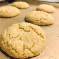 5 baked lemon cookies on parchment paper and cookie sheet with crackly top and light golden yellow color