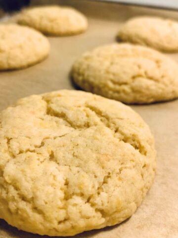 5 baked lemon cookies on parchment paper and cookie sheet with crackly top and light golden yellow color