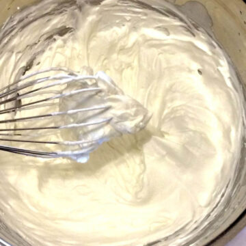 whipped cream in deep stainless steel bowl with balloon whisk lifting a small portion of cream out