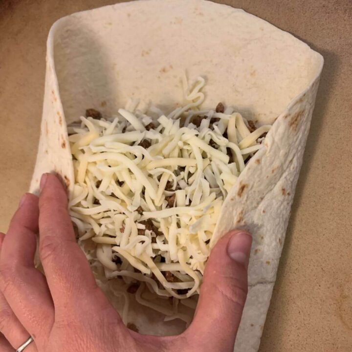 flour tortilla with ground beef mixture and shredded white cheese. Hand folding left and right edges in to filling.