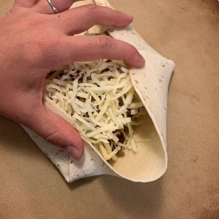 flour tortilla with ground beef mixture and shredded white cheese. Hand folding corner in to filling.