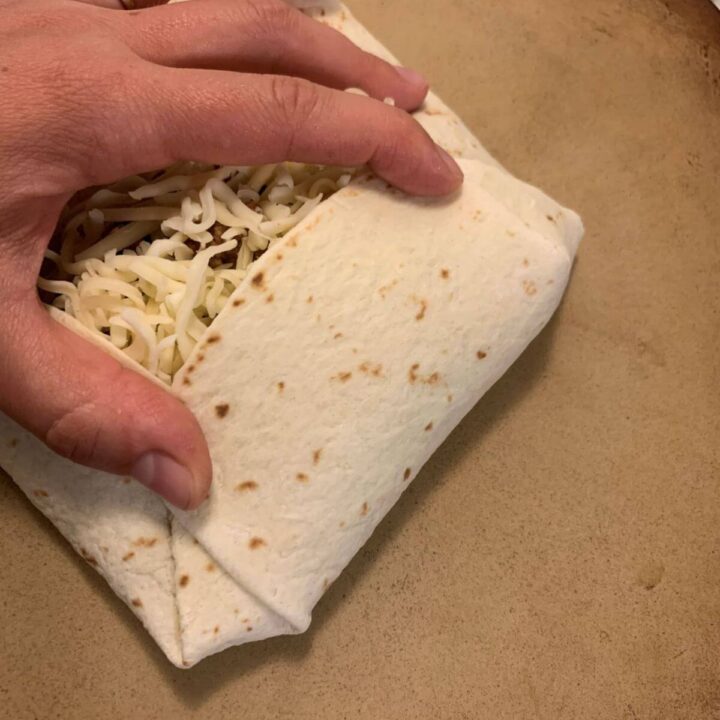 flour tortilla with ground beef mixture and shredded white cheese. Hand folding edge into filling.