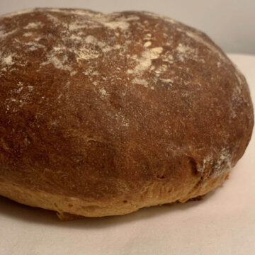 Side view of bloomer bread round with dark brown crust, dusted with flour on a white plate.
