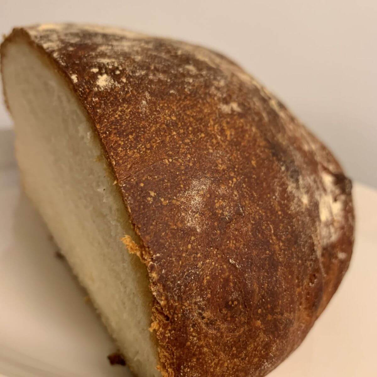 Bloomer bread without cuts with dark brown crust, side angle with bread cut open, on a white plate.