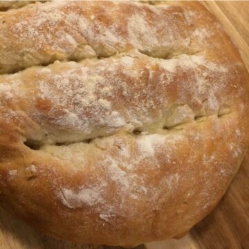bloomer bread with shallow cuts and over-proofed dough, baked with a lightly golden crust and flour dusting.