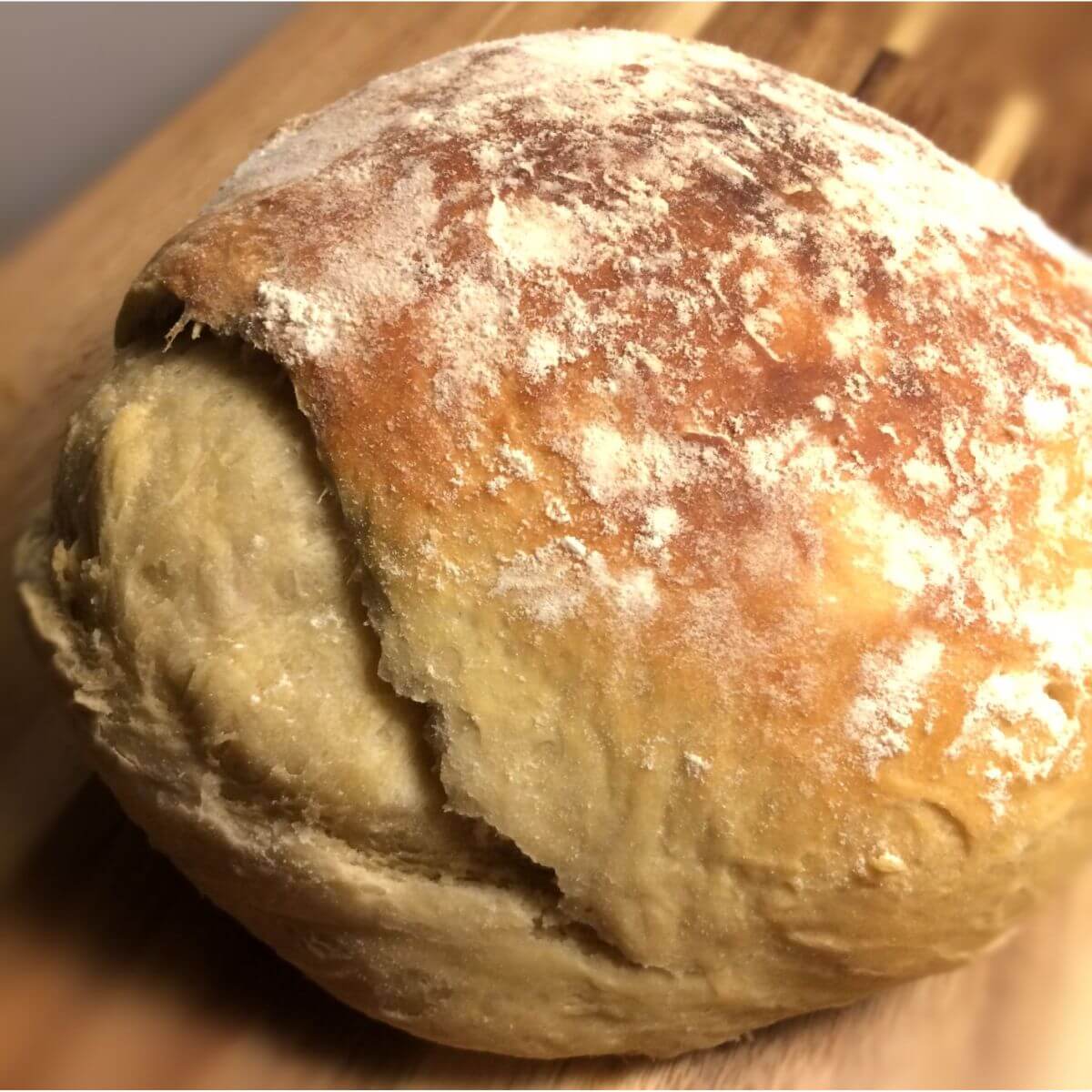 smaller bloomer bread round with light golden brown crust and flour dusting with the side burst open.