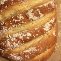 Bloomer bread in an elongated shape with light golen brown color, 6 diagonal slashes across the bread, flour dusting.