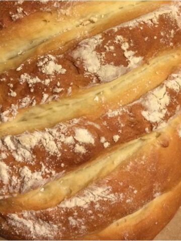 Bloomer bread in an elongated shape with light golen brown color, 6 diagonal slashes across the bread, flour dusting.