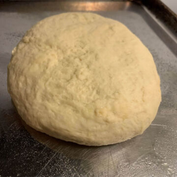 Bread dough formed ball on a stainless steel cookie sheet.