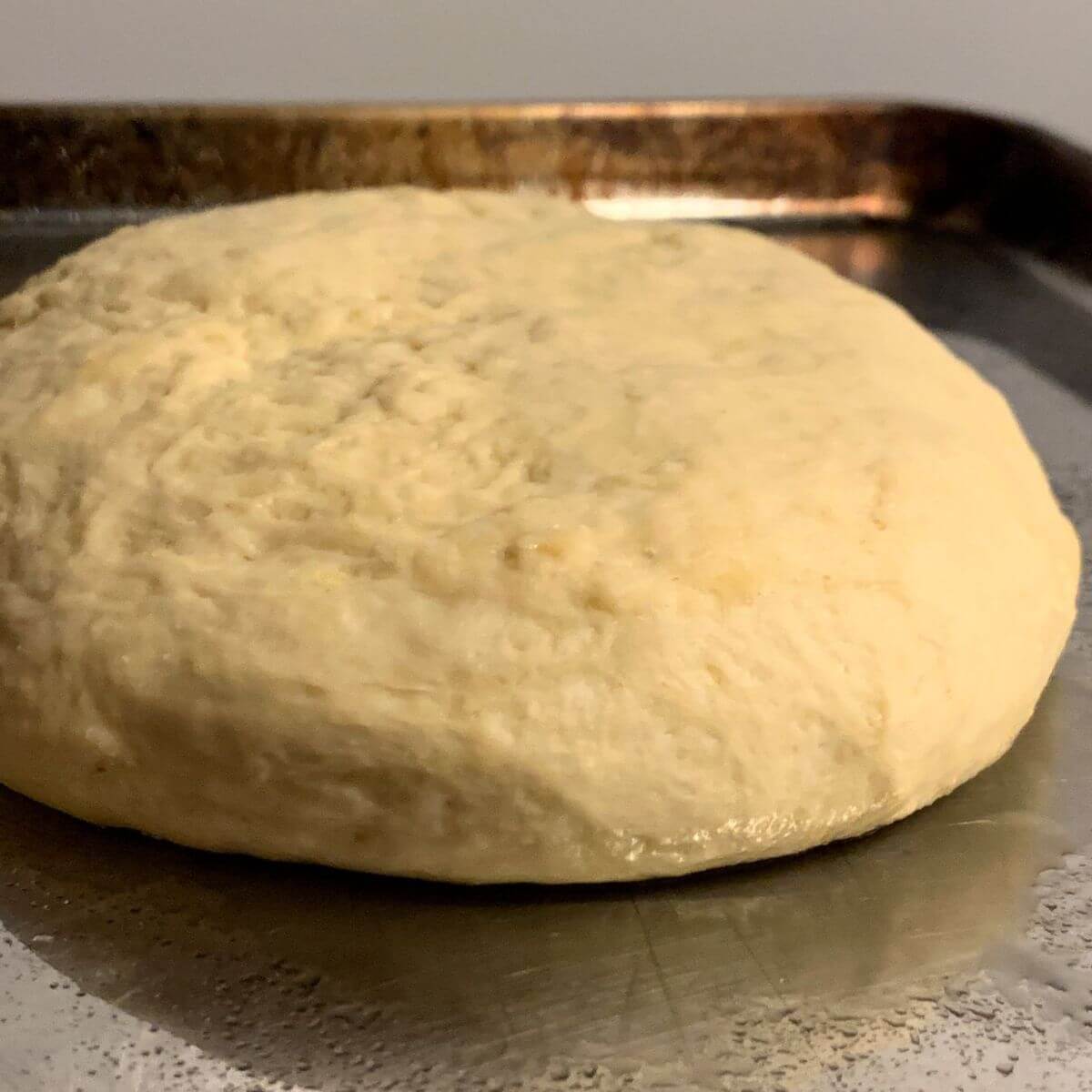 Side view of bread dough round risen on a stainless steel cookie sheet.