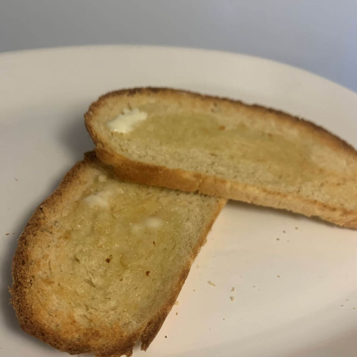 2 thin slices of bloomer bread made into toast with melted butter on top, on a white plate.