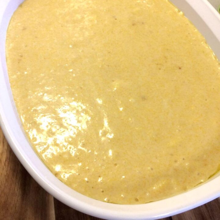 Batter for cornbread in a white CorningWare casserole dish on wooden cutting board.