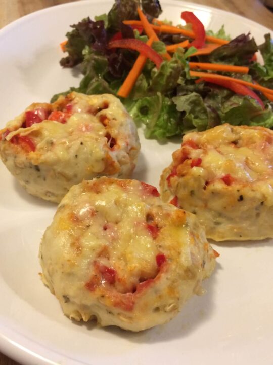 3 baked crustless strombolis topped with melted cheese and a side salad with sliced carrots and bell peppers on top, all on a white oval plate.