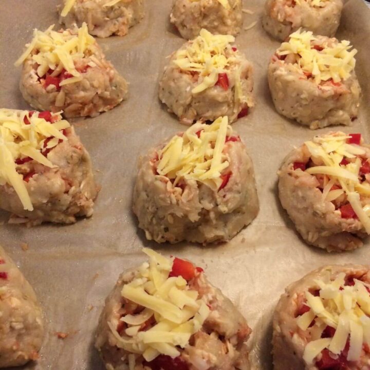 ground meat rolled around veggies topped with shredded cheese lined up on parchment paper.
