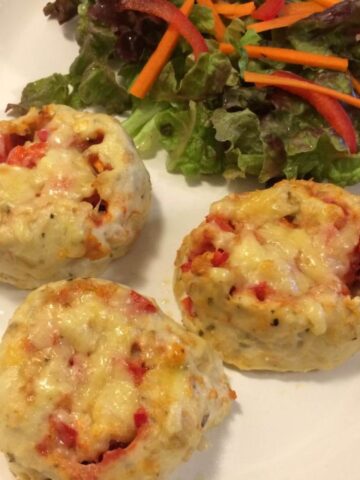 3 baked crustless strombolis topped with melted cheese and a side salad with sliced carrots and bell peppers on top, all on a white oval plate.