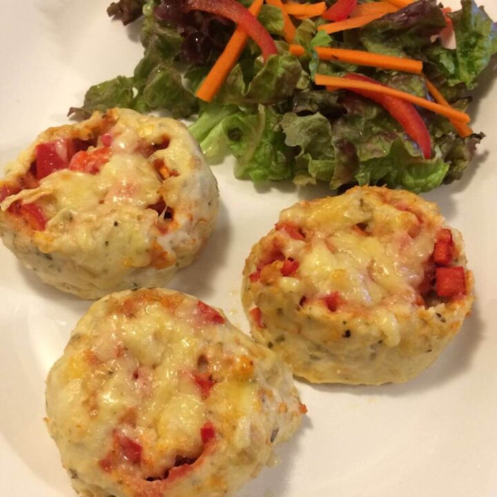 3 baked crustless strombolis topped with melted cheese and a side salad with sliced carrots and bell peppers on top, all on a white oval plate.