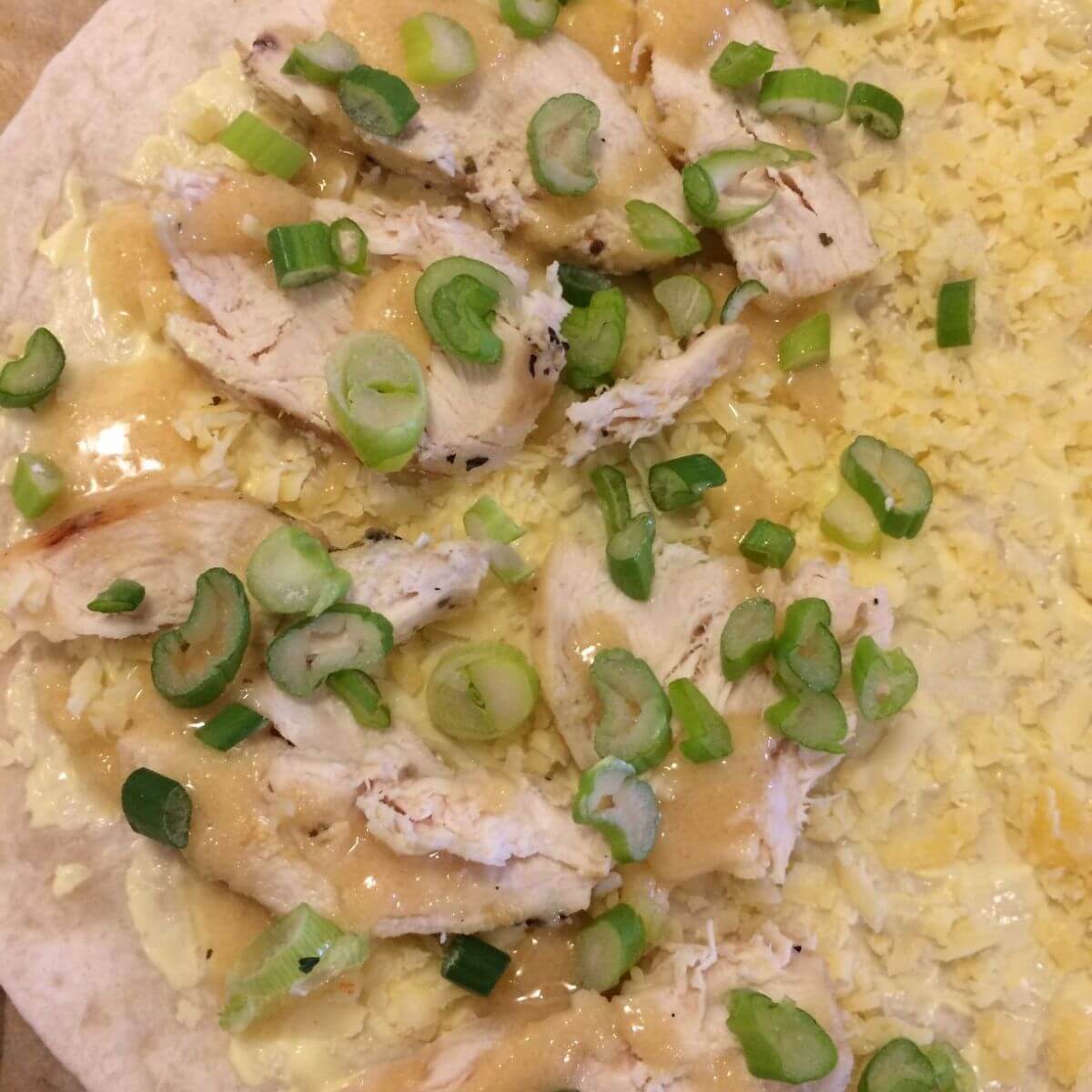 tortilla with shredded cheese, sliced green onions, chicken, and honey.