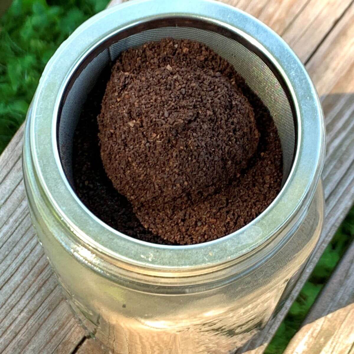 coffee grounds in mesh insert in mason jar, on a wooden table outside.