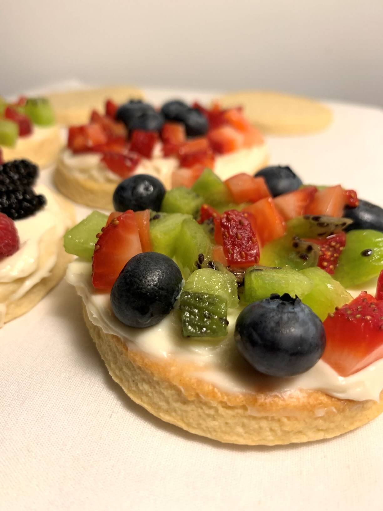 fruit pizza cookies with creamy frosting and fresh berries and died strawberries and kiwi on a white towel.