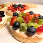 fruit pizza cookies with creamy frosting and fresh berries and died strawberries and kiwi on a white towel.