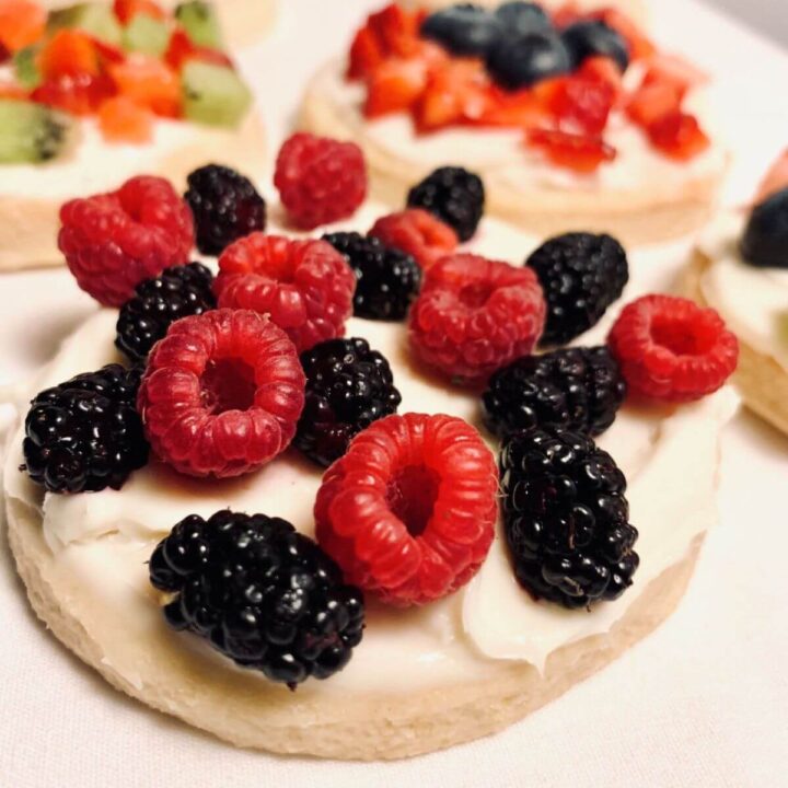 fruit pizza cookies with creamy frosting and fresh berries and died strawberries and kiwi on a white towel.