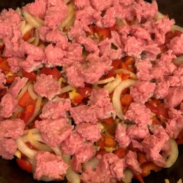 sliced onion, red bell pepper, diced garlic with chunks of uncooked ground pork in cast iron skillet.