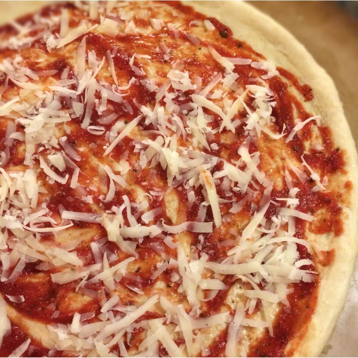 pizza dough, sauce, and shredded cheese on a pizza stone.