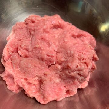 Ground pork for pork pasta pressed together into a round in a stainless steel bowl.