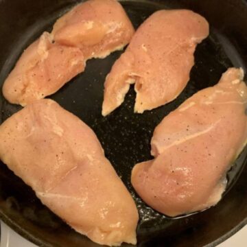Filleted chicken breasts in a cast iron skillet.