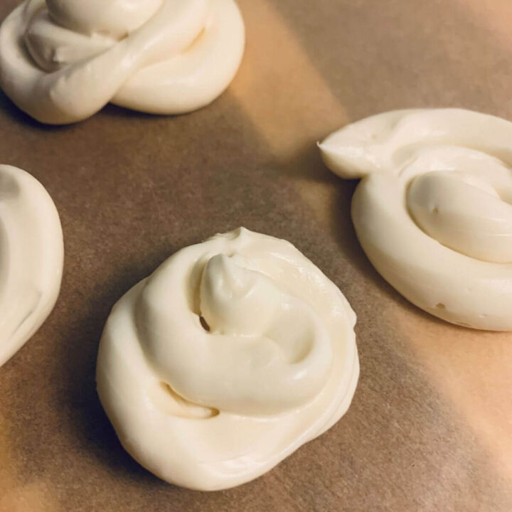 cream cheese frosting piped out into mounds on parchment paper over a wooden cutting board.