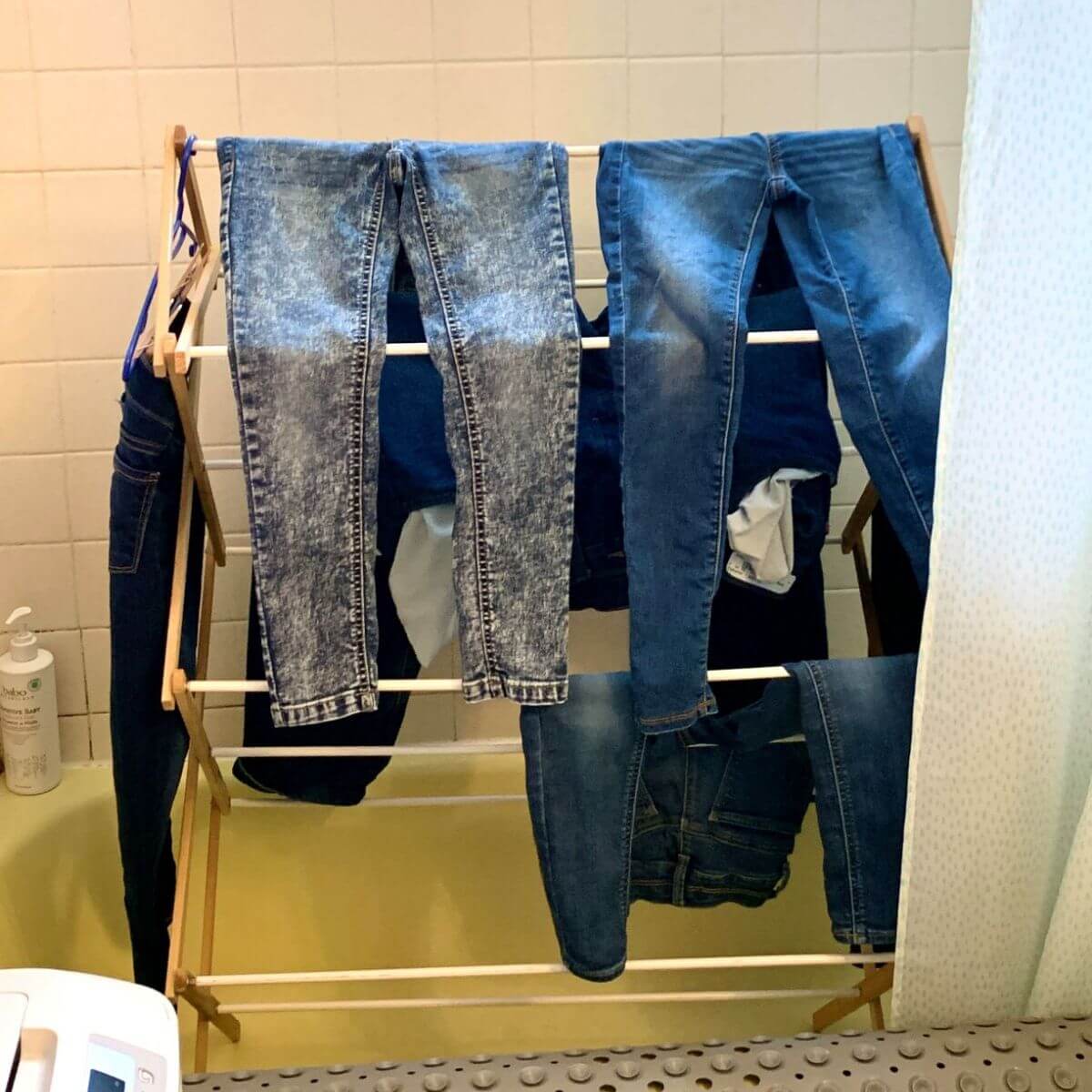 drying rack full of jeans in yellow bathtub.
