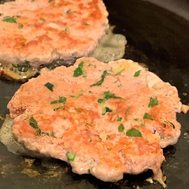 2 cooked turkey burger patties on cast iron skillet.