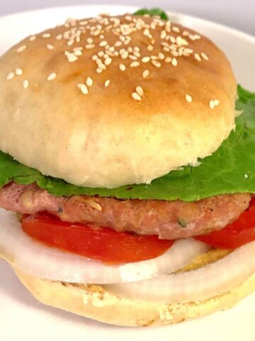 Square image of turkey burger with homemade buns with sesame seeds, mixed lettuce blend, sliced tomato, sliced onion, mustard, and turkey patty.