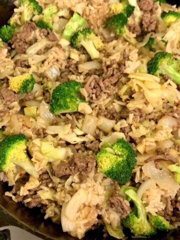 beef stir fry with rice, broccoli, cabbage, in cast iron skillet, close up square image.